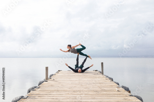 Couple practicing acroyoga on a dock on a lake