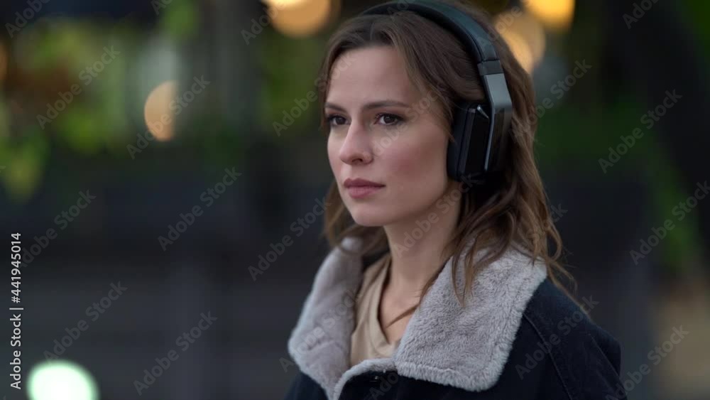 portrait of a serious woman wearing headphones against the background of blurred sun glare. she pulls up her fur collar portrait of a serious woman wearing headphones against the background of blurred sun glare. she pulls up her fur collar