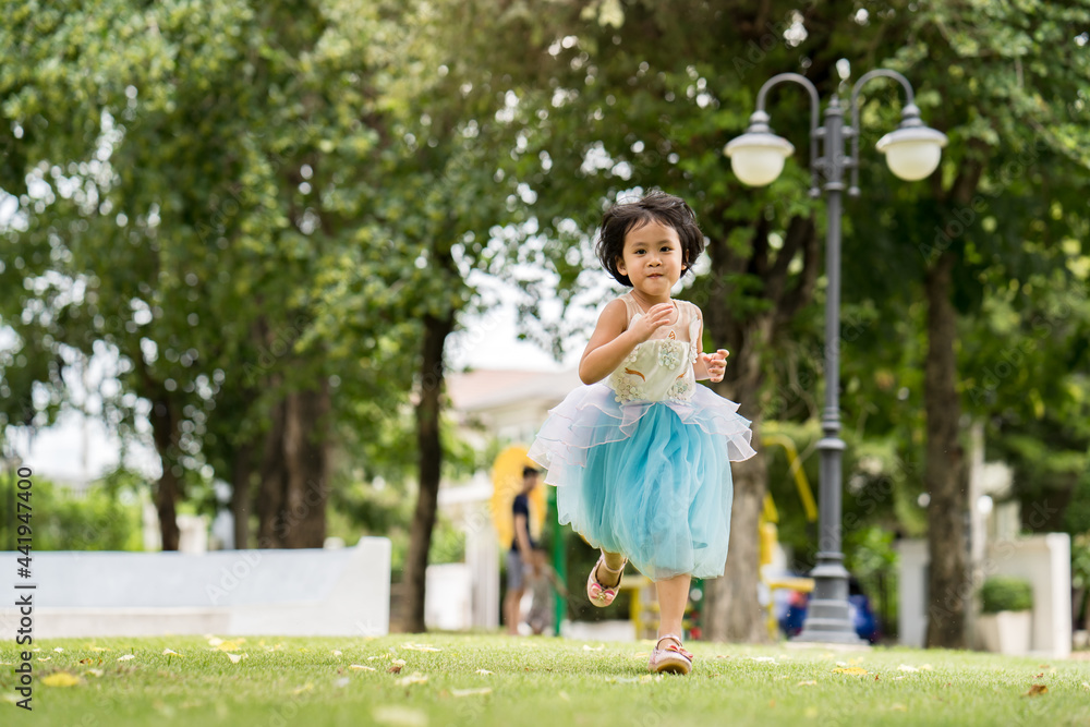 Adorable little Asian girl in blue dressed running at park.