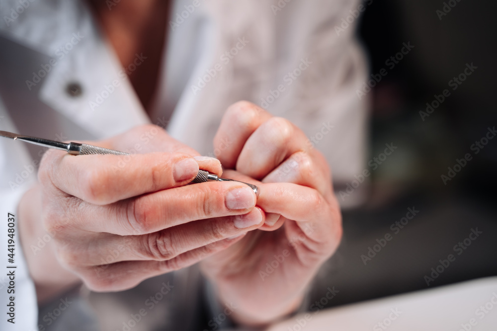 Home manicure. In the photo, a woman in a white coat is using a cuticle lifting tool.