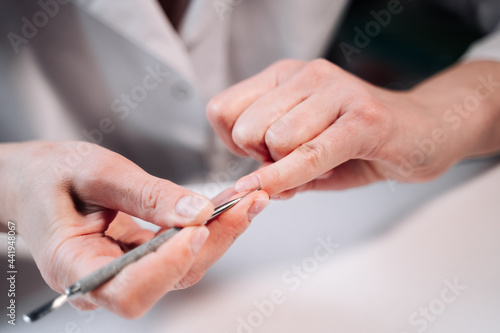 Home manicure. In the photo  a woman in a white coat is using a cuticle lifting tool.