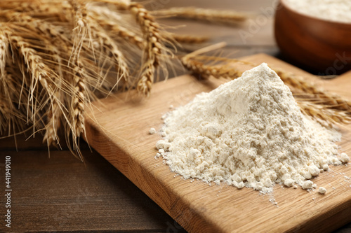 Pile of flour and wheat ears on wooden table, closeup photo