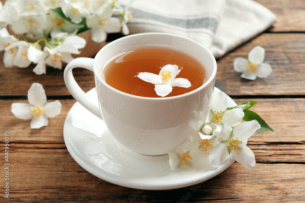 Cup of aromatic jasmine tea and fresh flowers on wooden table Cup of aromatic jasmine tea and fresh flowers on wooden table