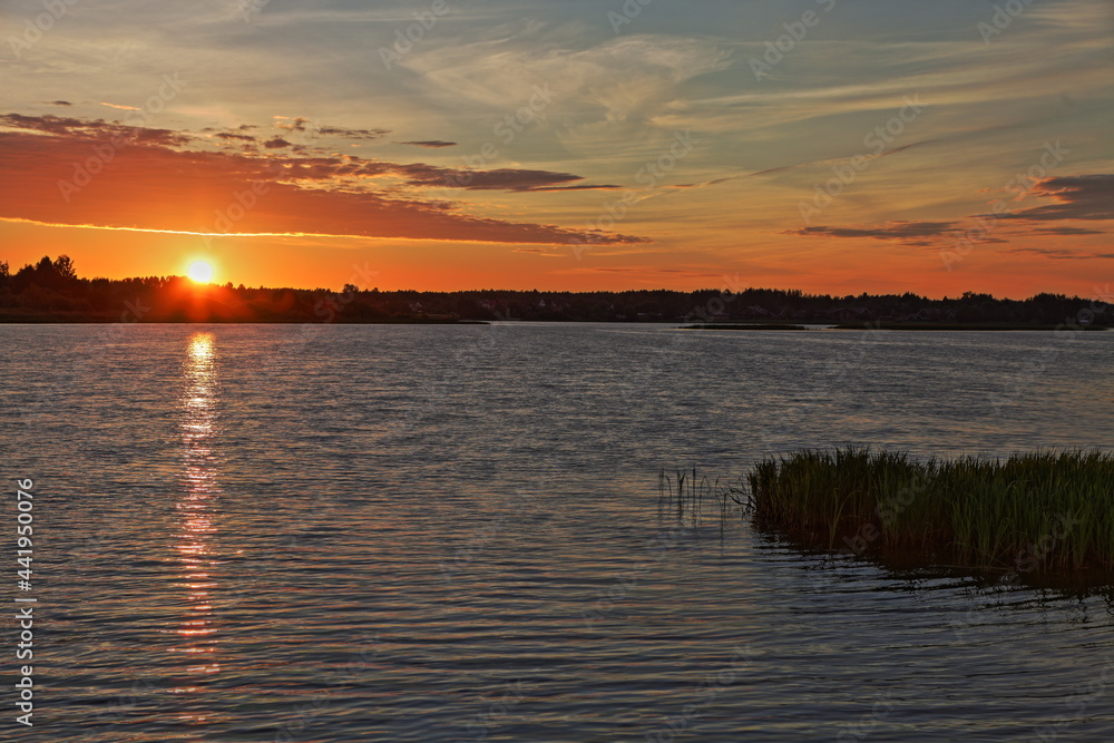 Beautiful orange sunrise in Russia on Volga River calm water with a Sun glow in the sky and a forest stripe on the horizon in the calm water reflection on a summer morning, Russian natural landscape