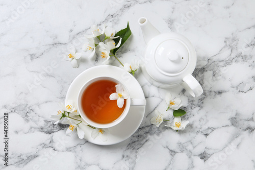 Aromatic jasmine tea and fresh flowers on white marble table, flat lay