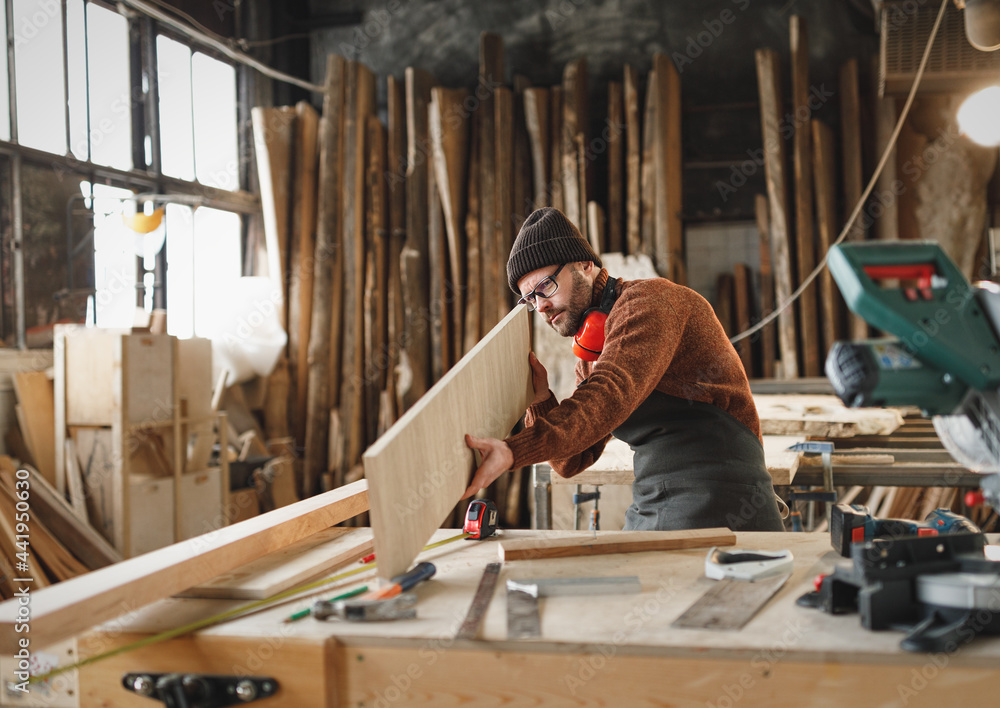 Craftsman examining wooden plank in workshop - obrazy, fototapety, plakaty 