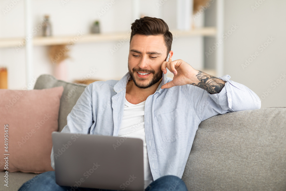 Always in touch. Young freelancer man talking on smartphone and using laptop while working remotely from home Always in touch. Young freelancer man talking on smartphone and using laptop while working remotely from home