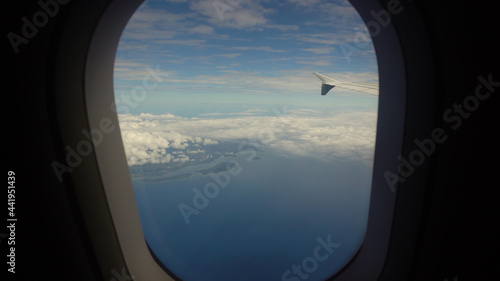 Airplane flying over blue sea and tropical island. Airplane wing through the porthole. Looking through window aircraft during flight