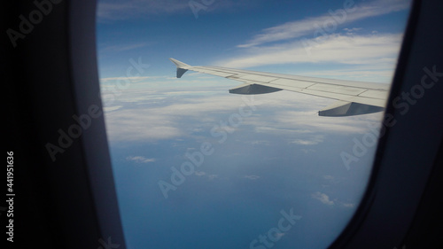 Airplane flying over blue sea and tropical island. Airplane wing through the porthole. Looking through window aircraft during flight