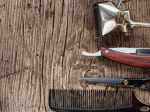 On a old wooden surface are old barber tools. Vintage manual hair clipper comb razor shaving hairdressing scissors