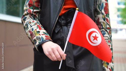 Unrecognizable woman holding Tunisian flag. Girl walking down street with national flag of Tunisia