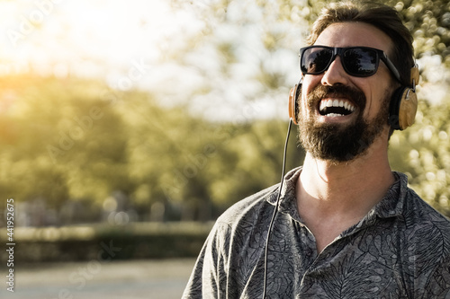 Hipster man listening music while wearing headphones outdoor during summer vacation - Focus on face