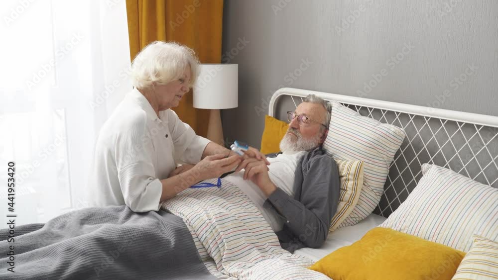 Elderly woman apply at sick husband's fingertip pulse oximeter, check pulse rate. man lying on