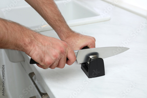 Man sharpening knife at white table indoors, closeup