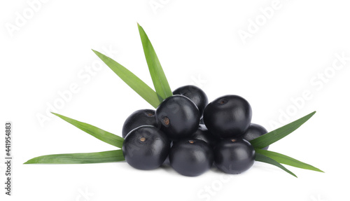 Pile of fresh ripe acai berries and green leaves on white background