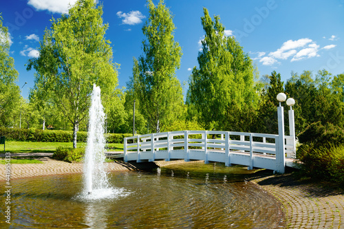 A beautiful park with a pond, wooden bridge and fountain in sunny summer day photo