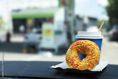 Fototapeta Naklejka Na Ścianę i Meble -  Paper coffee cup and doughnut on car dashboard at gas station