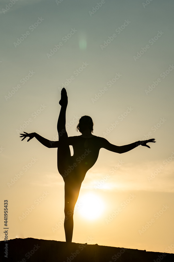 Silhouette of flexible and fit girl keeping balance in split on sunset background. Concept of yoga, meditation and healthy lifestyle 
