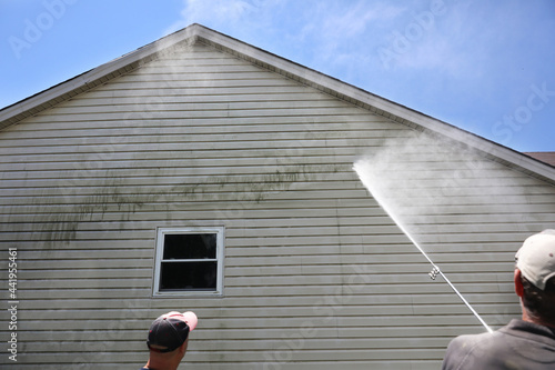 Mold is professionally cleaned from the side of a house using a pressure washer.