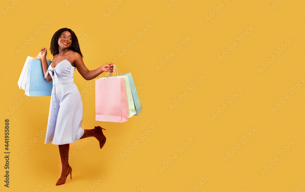 Full length of carefree black woman in dress running with bright shopping bags over orange background, free space Full length of carefree black woman in dress running with bright shopping bags over orange background, free space