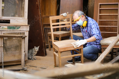 Senior Asian carpenter man is repairing wooden chair in his own garage style workshop at retirement age for hobby