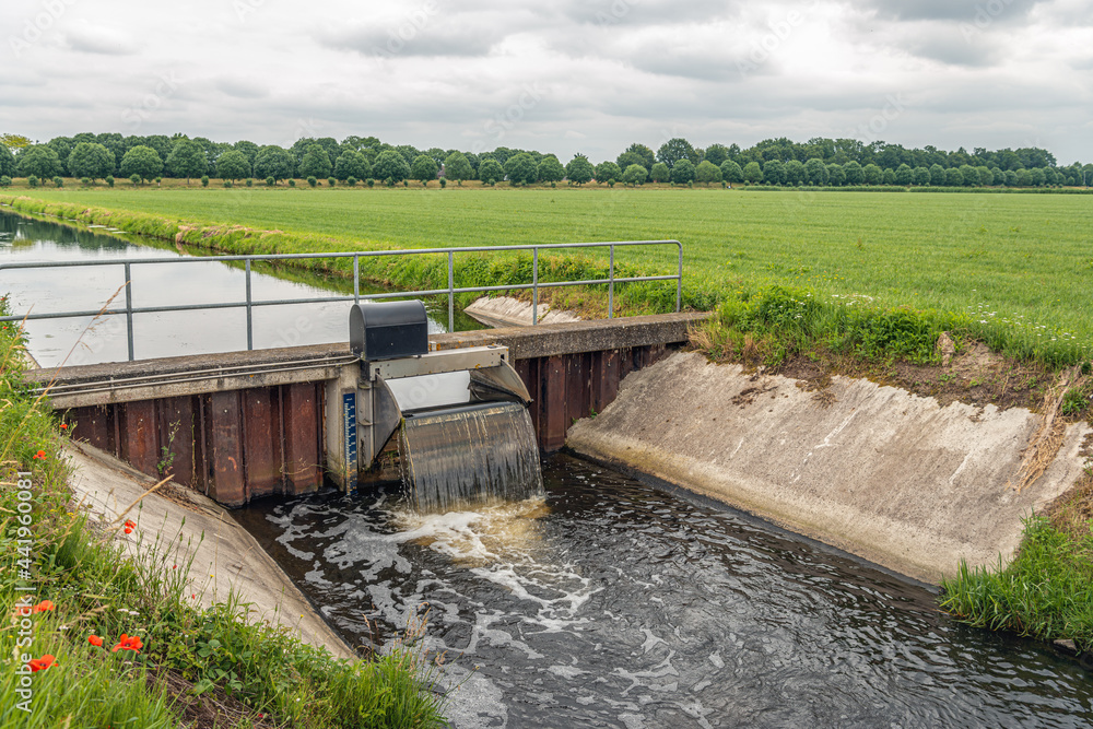 The water foams at the overflowing weir in a Dutch polder landscape. The small weir keeps the water at the right level in the agricultural polder area.