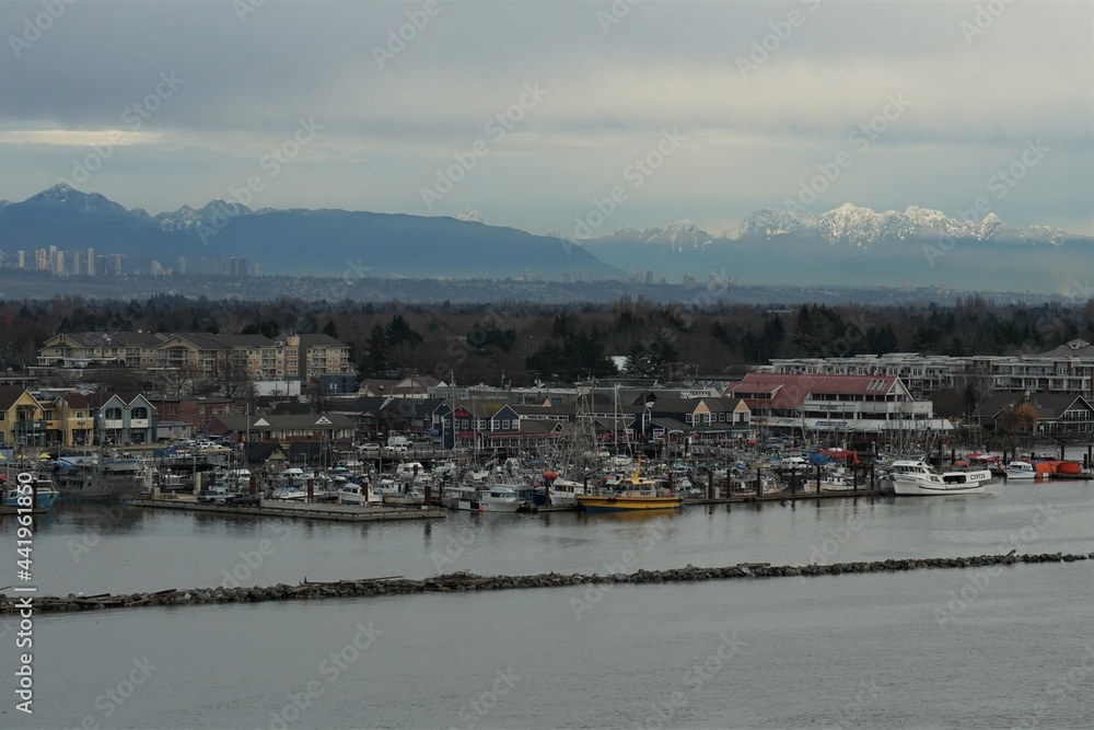 Fishing village of Steveston with boats on the Fraser river in , typical port town in west Canada connected with Pacific Ocean. View from container vessel and on the background are mountains.