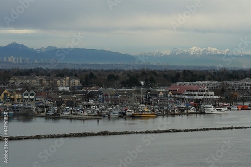 Fishing village of Steveston with boats on the Fraser river in , typical port town in west Canada connected with Pacific Ocean. View from container vessel and on the background are mountains. photo