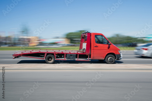 A red tow truck is driving down the street at high speed. Motion blur
