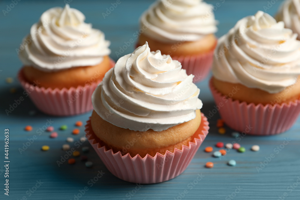 Delicious cupcakes decorated with cream on light blue wooden table, closeup Delicious cupcakes decorated with cream on light blue wooden table, closeup