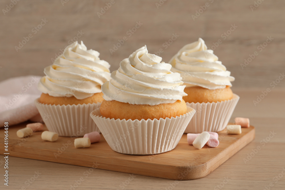 Delicious cupcakes with cream and marshmallows on wooden table