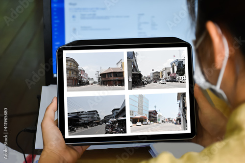 An office lady holding a tablet in hands and looking at video streaming from CCTV traffic cameras which installed beside the main road before going back home. Soft and selective focus on taplet.