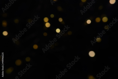 Defocused bokeh christmas small gold lights on black background. Blurred abstract yellow glitter texture. Gold bokeh glitter wallpaper for Christmas, New year, festival background.