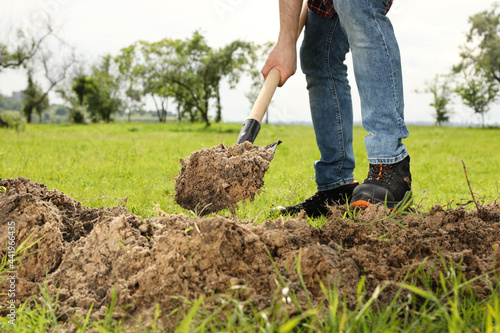 Worker digging soil with shovel outdoors, closeup