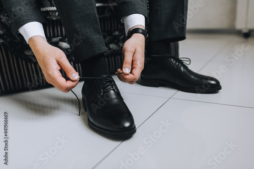 A man, a businessman, ties long shoelaces on leather black shoes, shiny with cream, with his hands in a jacket close-up. Advertising photography.