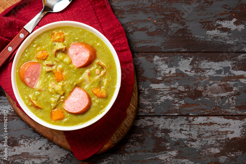Green pea soup with carrots, potatoes, celery, sausages, pork and bacon in a white bowl on a dark wooden background. Snert is a Dutch pea soup.