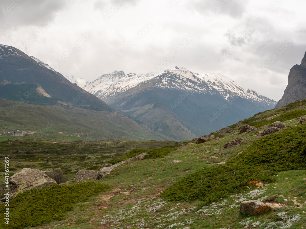 Fototapeta premium View of the green valley from the main attraction of the village of Eltyubyu, the City of the Dead. High snowy mountains are visible on the horizon. Kabardino-Balkaria, Russia