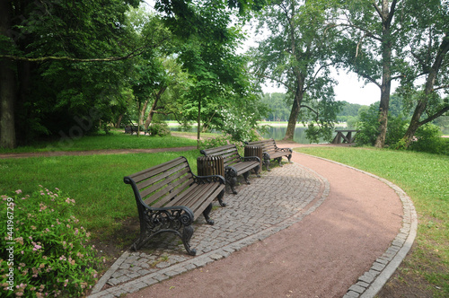 Panoramic view of the city park. Garden benches against the backdrop of a park path and a pond.
