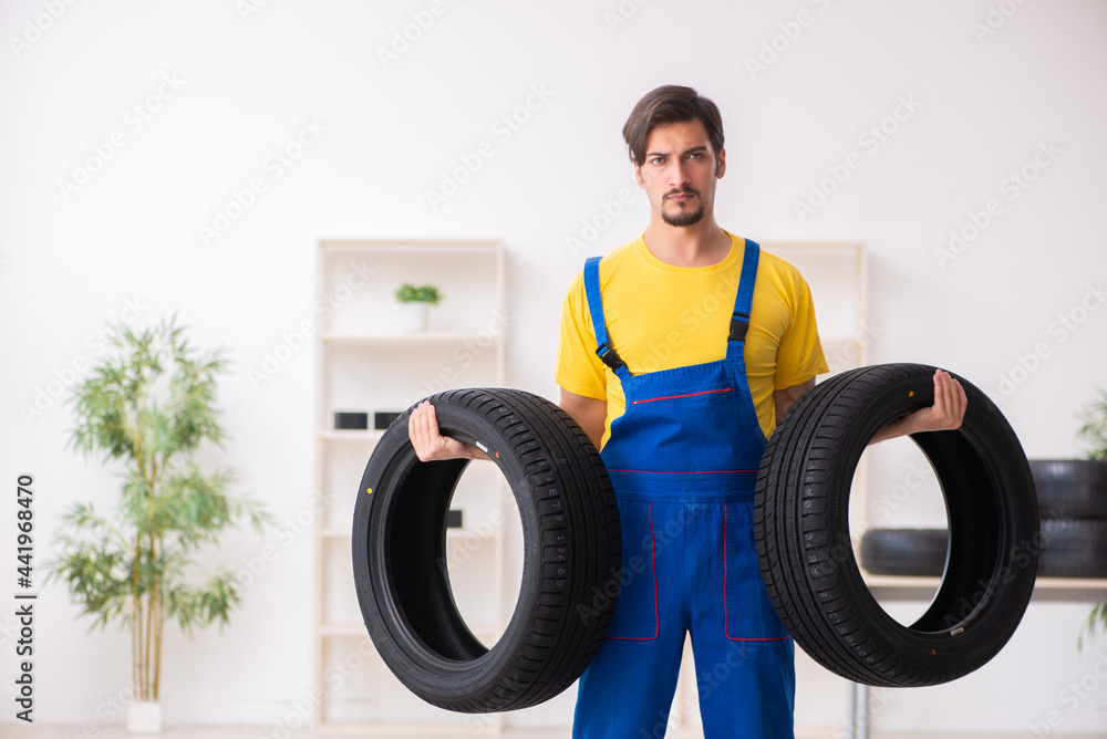 Young male garage worker with tyre at workshop Young male garage worker with tyre at workshop