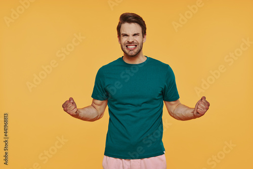 Furious young man in casual clothing making a face while standing against yellow background
