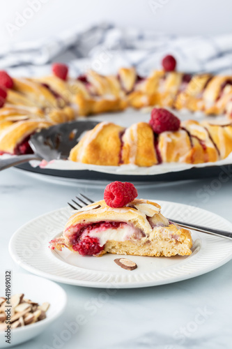 Close up view of a slice from a raspberry crescent ring with the full ring in behind.