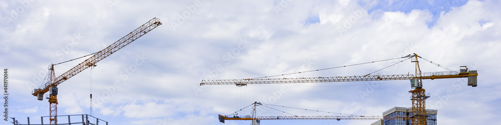 Construction cranes on the background of the sky with clouds. Panoramic image.