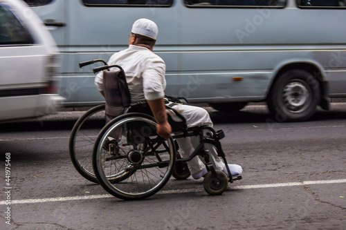 A man in a wheelchair asks for alms from the drivers of the main city highway.