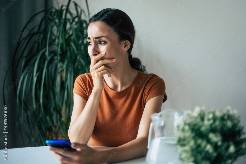 Sad, frustrated young woman is crying with smartphone in hands