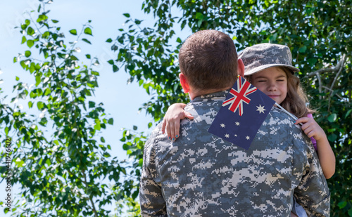 Reunion of soldier from Australia with family, daughter hug father. A girl holds the flag of Australia in her hand