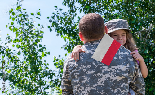 Reunion of soldier from Poland with family, daughter hug father. A girl holds the flag of Poland in her hand