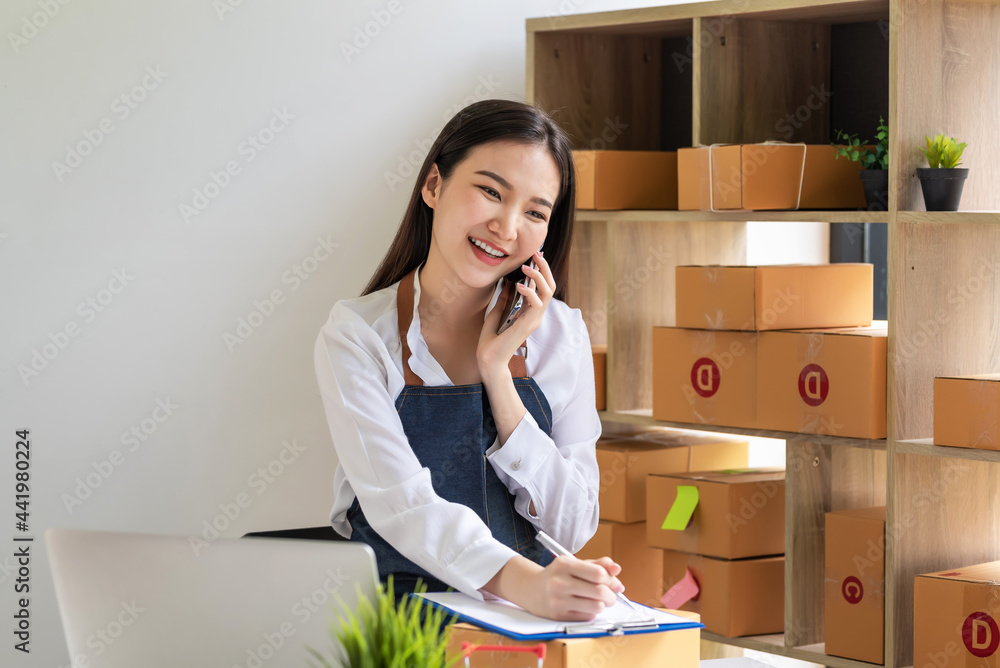 Small business owner Asian woman enjoys talking on the phone receive online sales orders taking notes at home. Small business owner Asian woman enjoys talking on the phone receive online sales orders taking notes at home.