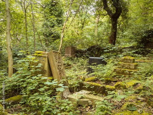 A vandalised Celtic Cross memorial lies broken in a neglected and overgrown burial ground
