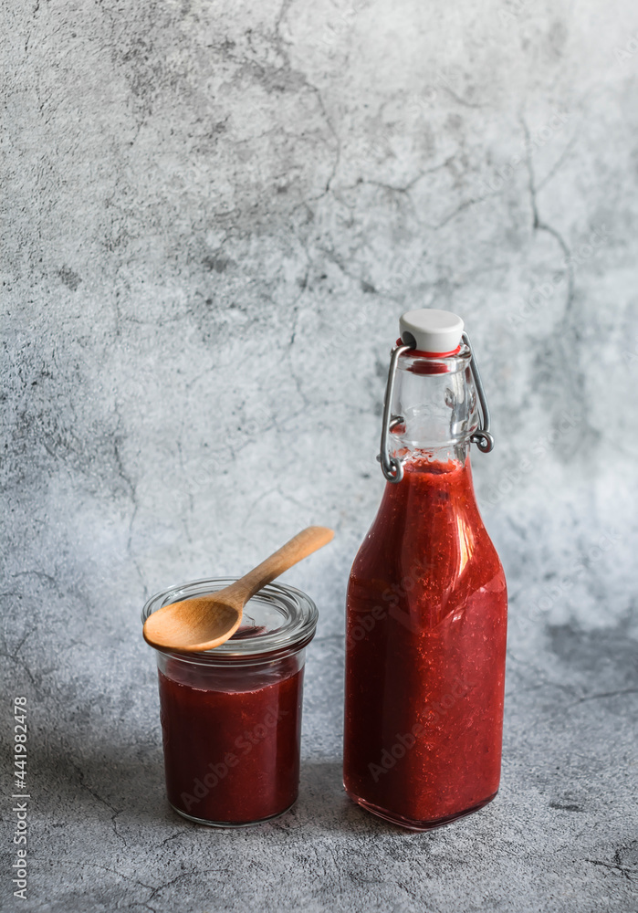 Obraz premium Rhubarb and strawberry sweet sauce in a canned bottle on a gray background. Free space for text