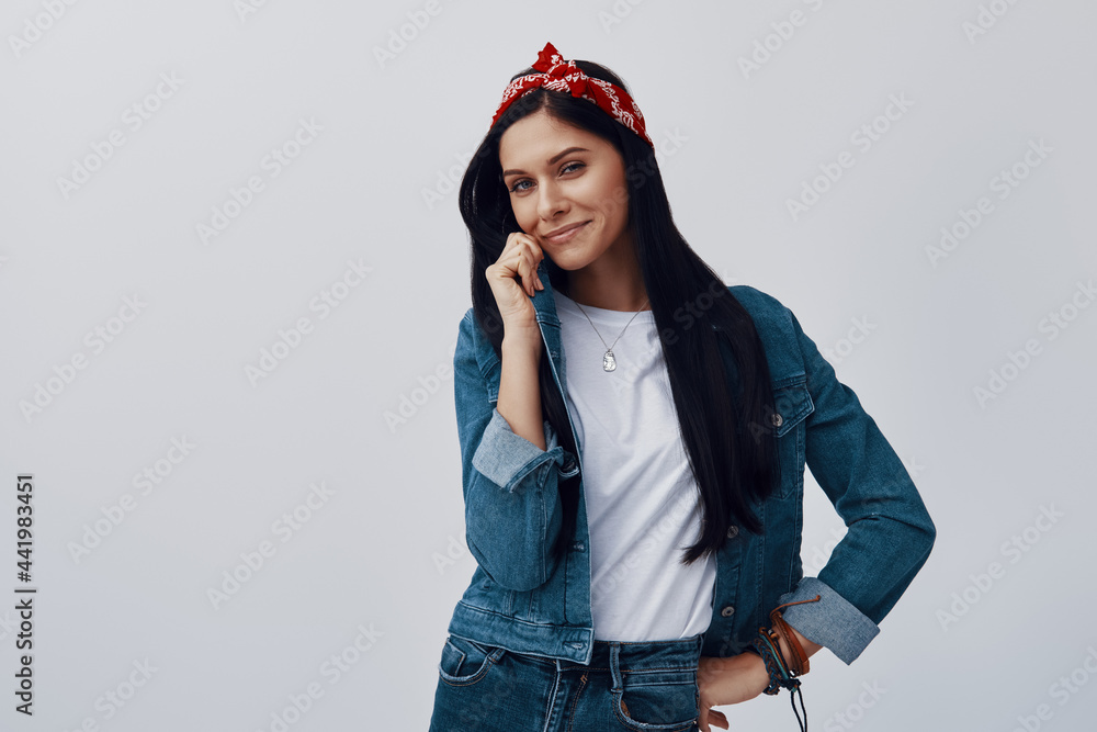 Attractive young woman in bandana looking at camera and smiling while standing against grey background